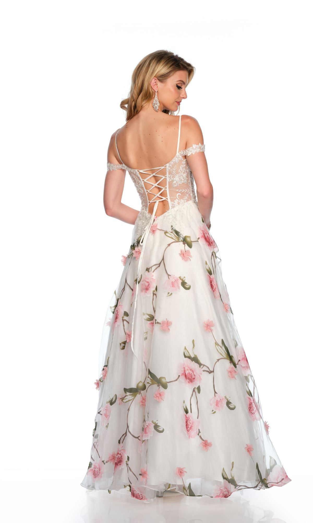A woman models the Dave & Johnny Long Prom Dress 11656—a white floral gown with a sweetheart neckline, lace-up back, pink accents, and an off-the-shoulder design—facing away from the camera.